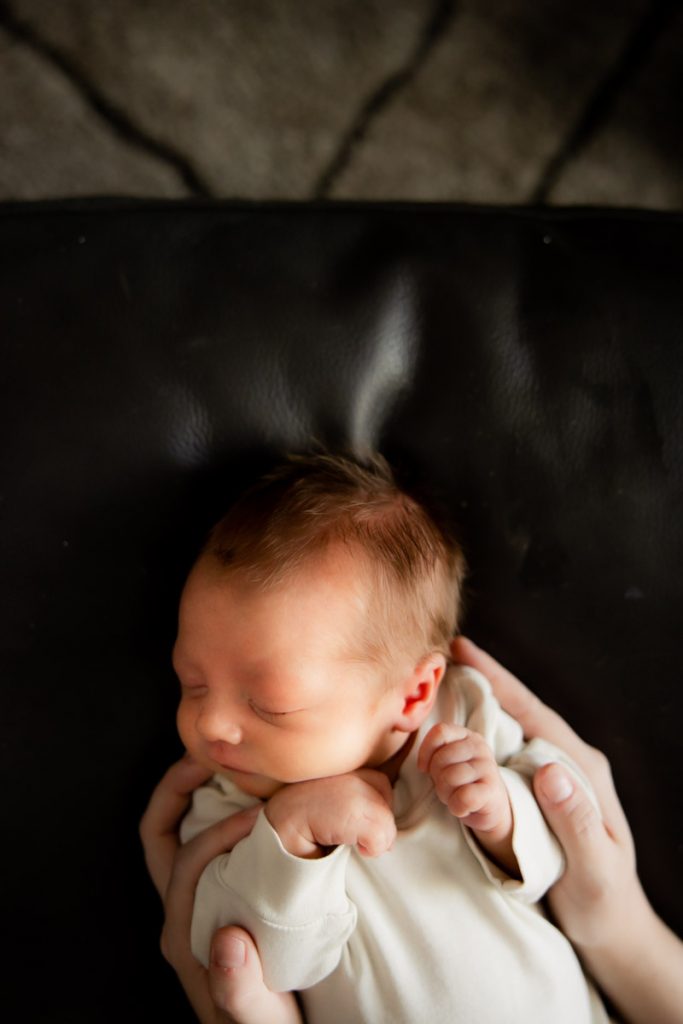 Newborn baby on black leather ottoman.