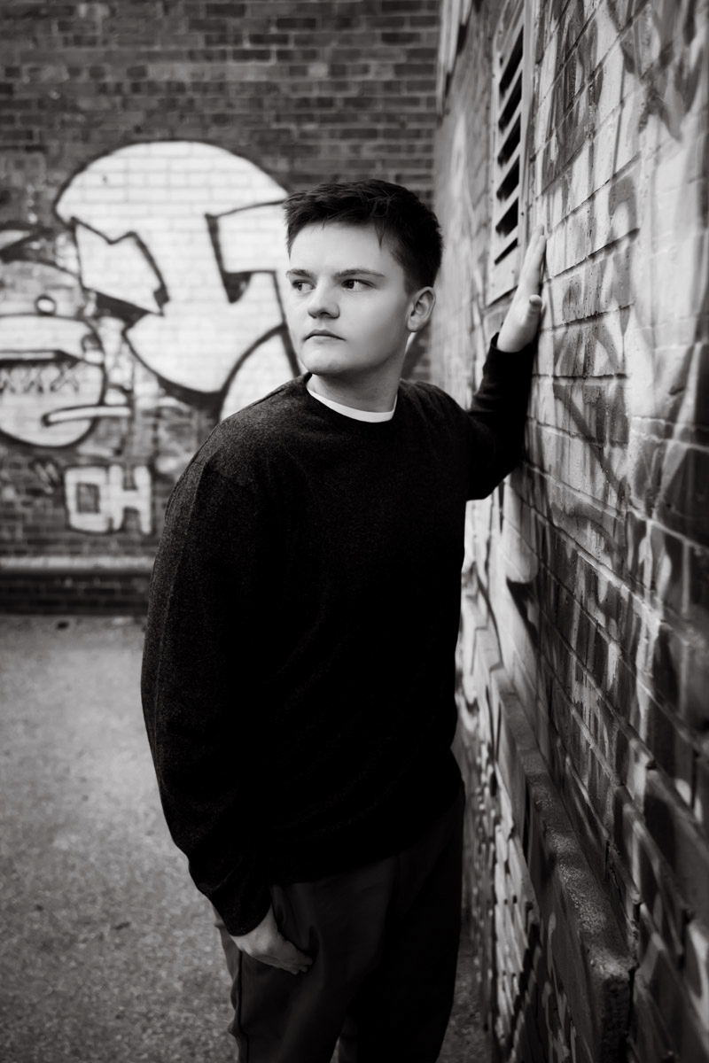 Senior leaning against a graffiti wall