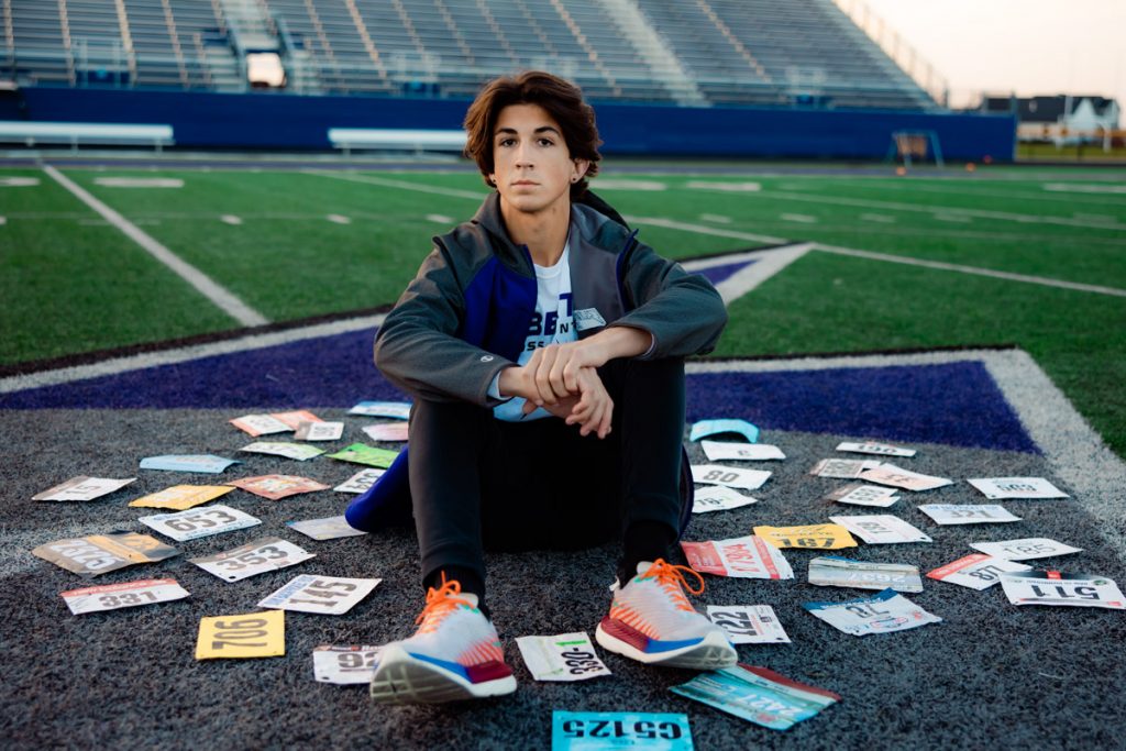 Senior boy surrounded by race bibs on a football field
