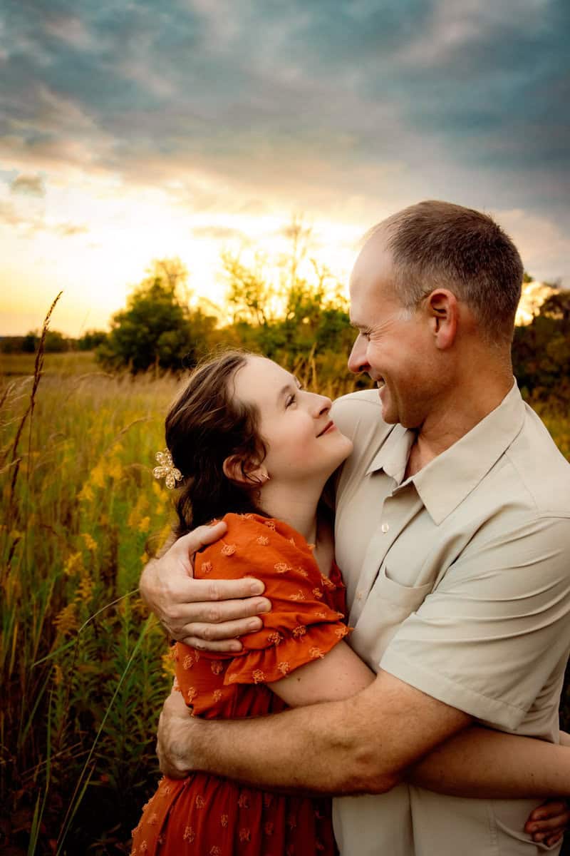 Best timing for family pictures: A month-by-month guide Dad and teen daughter embracing at sunset in a grassy field with wildflowers
