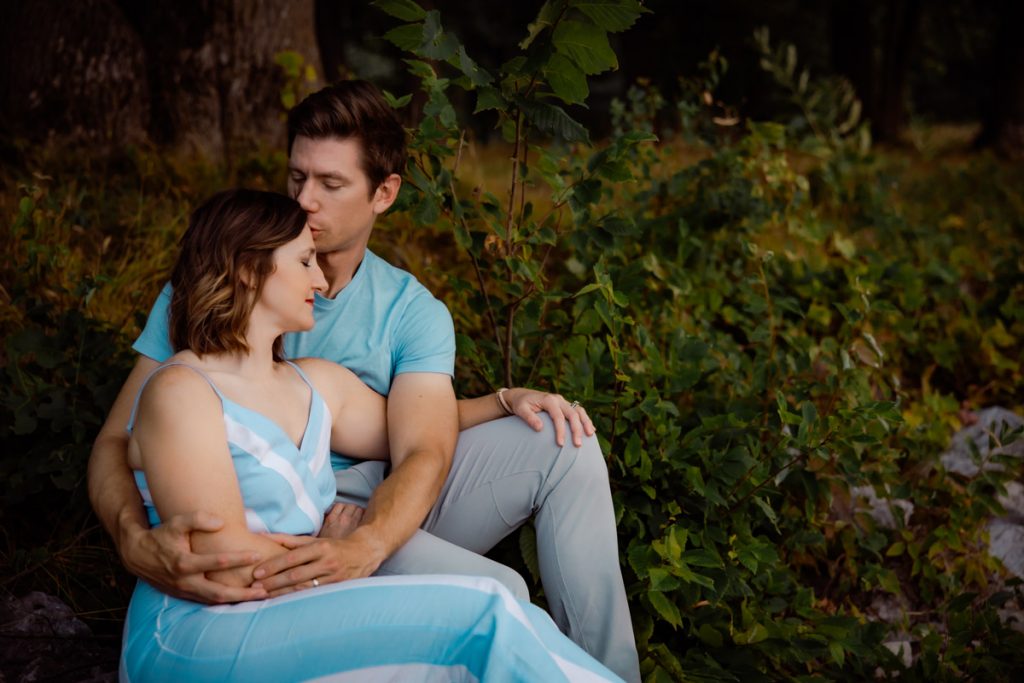 Husband kissing wife on the forehead while sitting alongside a lake