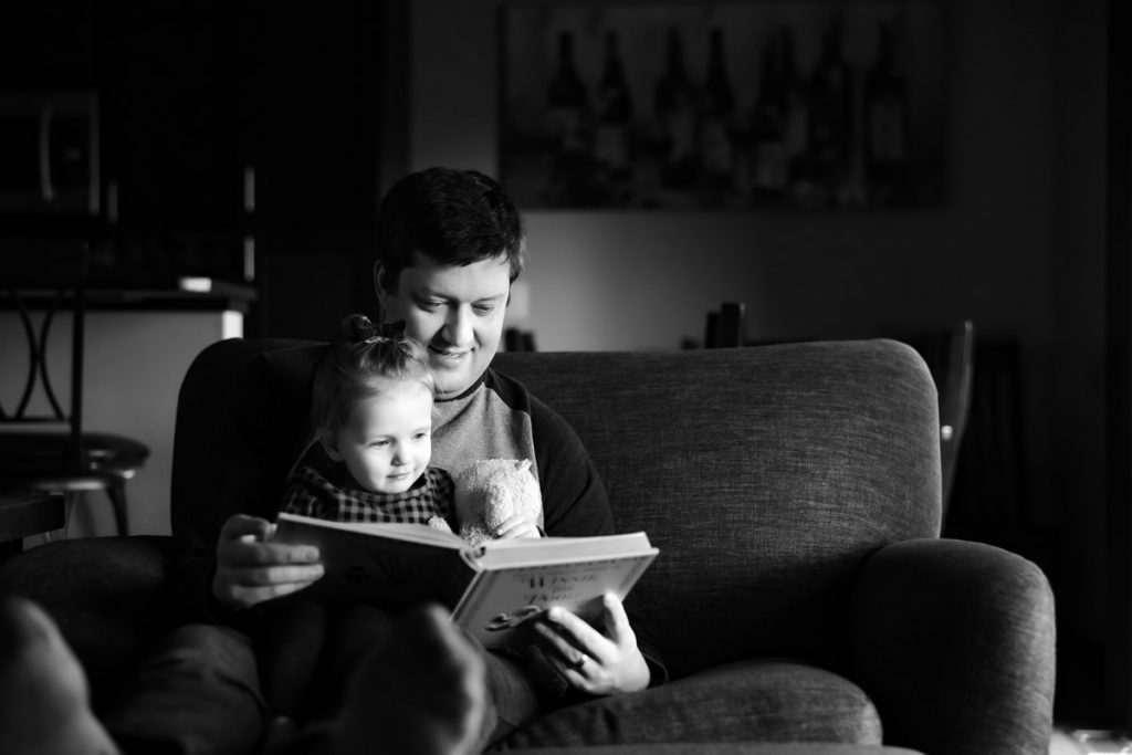 Dad with toddler girl on his lap, reading a book.