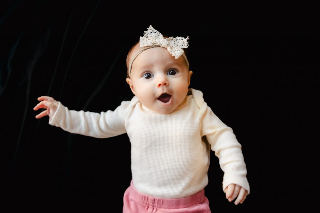 Fine Art School Photography Baby girl lying on a black background with a bow in her hair.