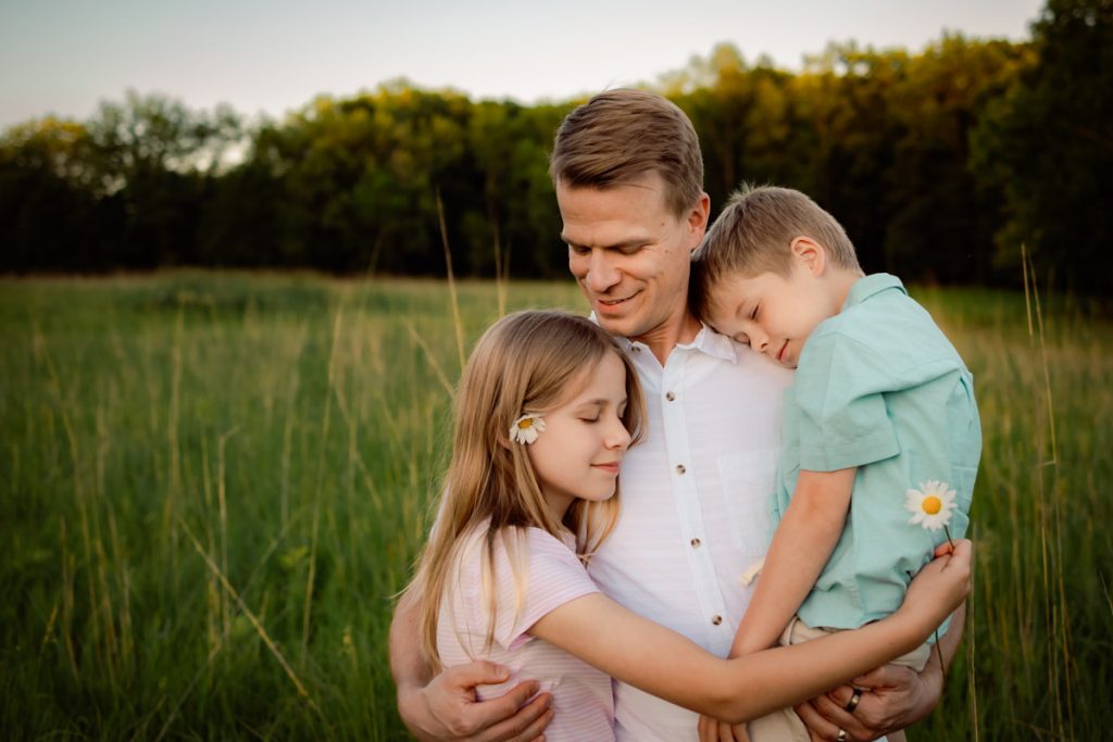 Dad holding son and embracing daughter in grassy field.