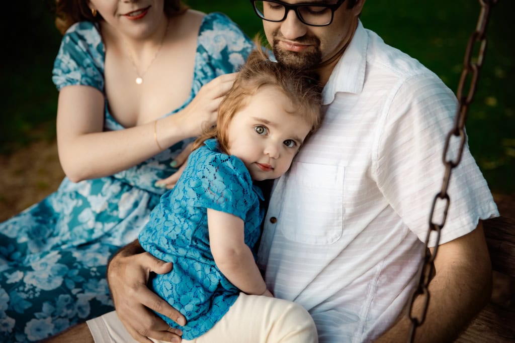 Best timing for family pictures: A month-by-month guide Toddler girl held by dad in a blue dress while sitting on a swing
