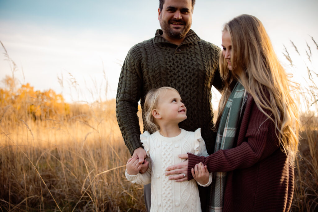What to wear for cold-weather outdoor photos Photo of a family standing in a grassy field wearing sweaters and fall outfits.