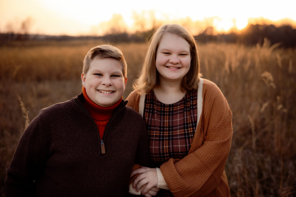 What to wear for cold-weather outdoor photos Photo of two teen siblings dressed for fall in layers, standing in a grassy field.