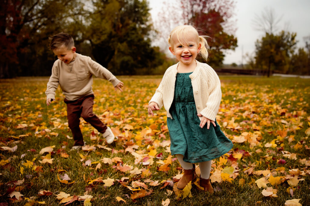 What to wear for cold-weather outdoor photos Photo of two young toddlers on a windy fall day, walking through bright yellow leaves dressed for fall.