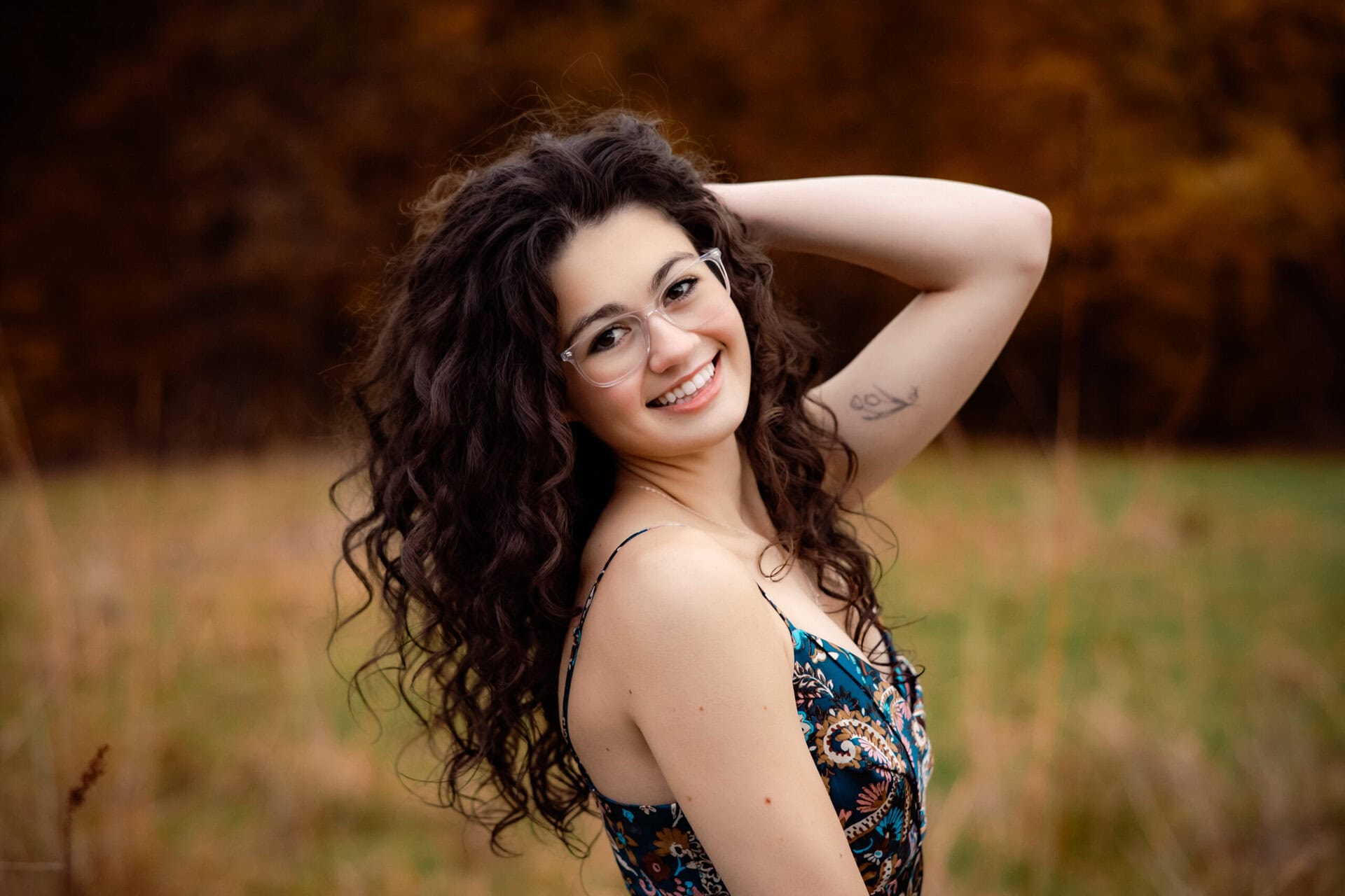 Senior girl with curly black hair in a spaghetti strap dress standing in a grassy field