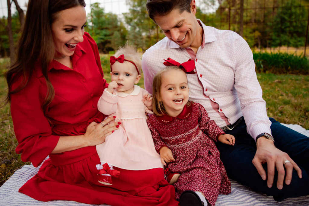 Family of four with two toddler girls, dressed in pinks and reds in a grassy area in Iowa