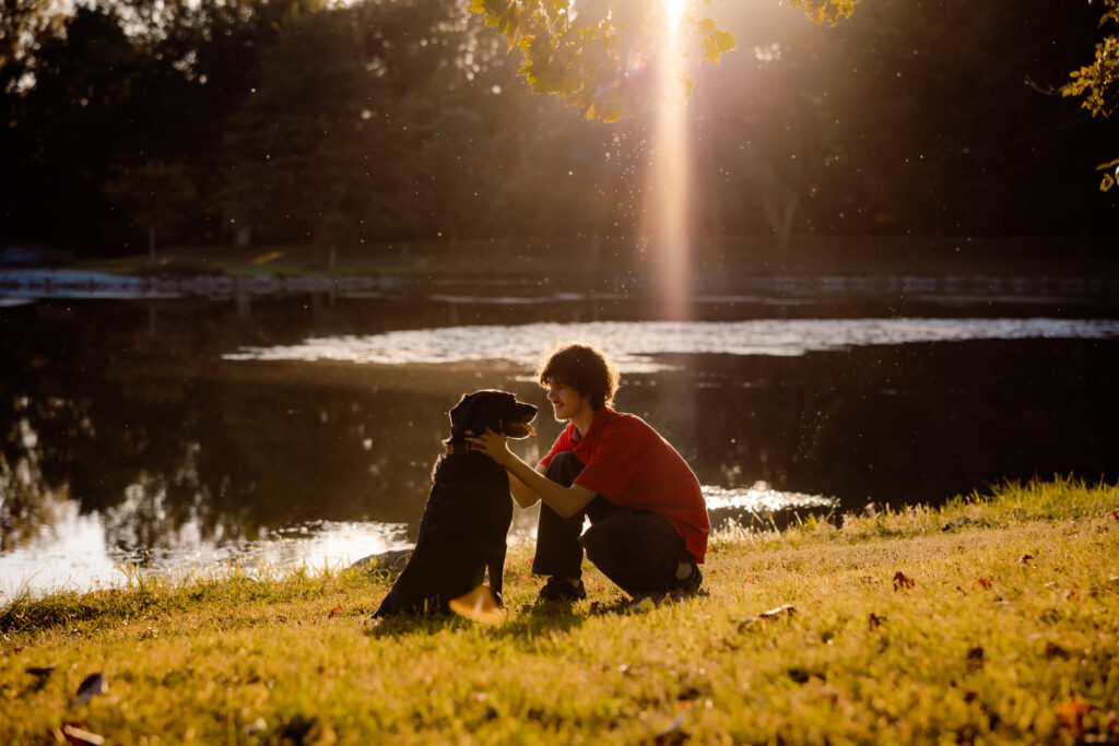 Beginner's guide to senior pictures in Iowa Senior boy crouching next to a lake with his black lab during golden hour