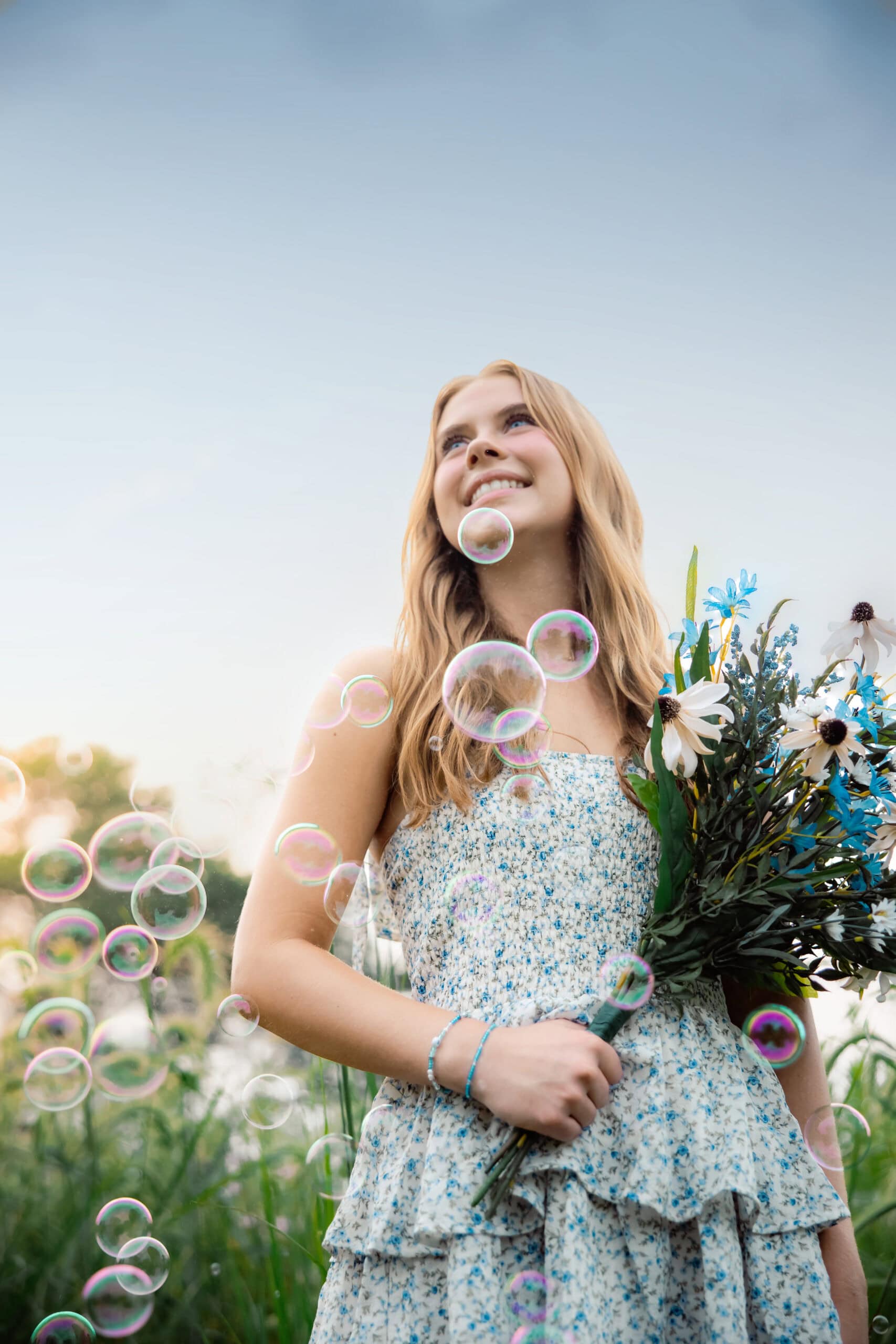 Senior girl holding a bouquet of flowers surrounded by bubbles against a dark blue sky