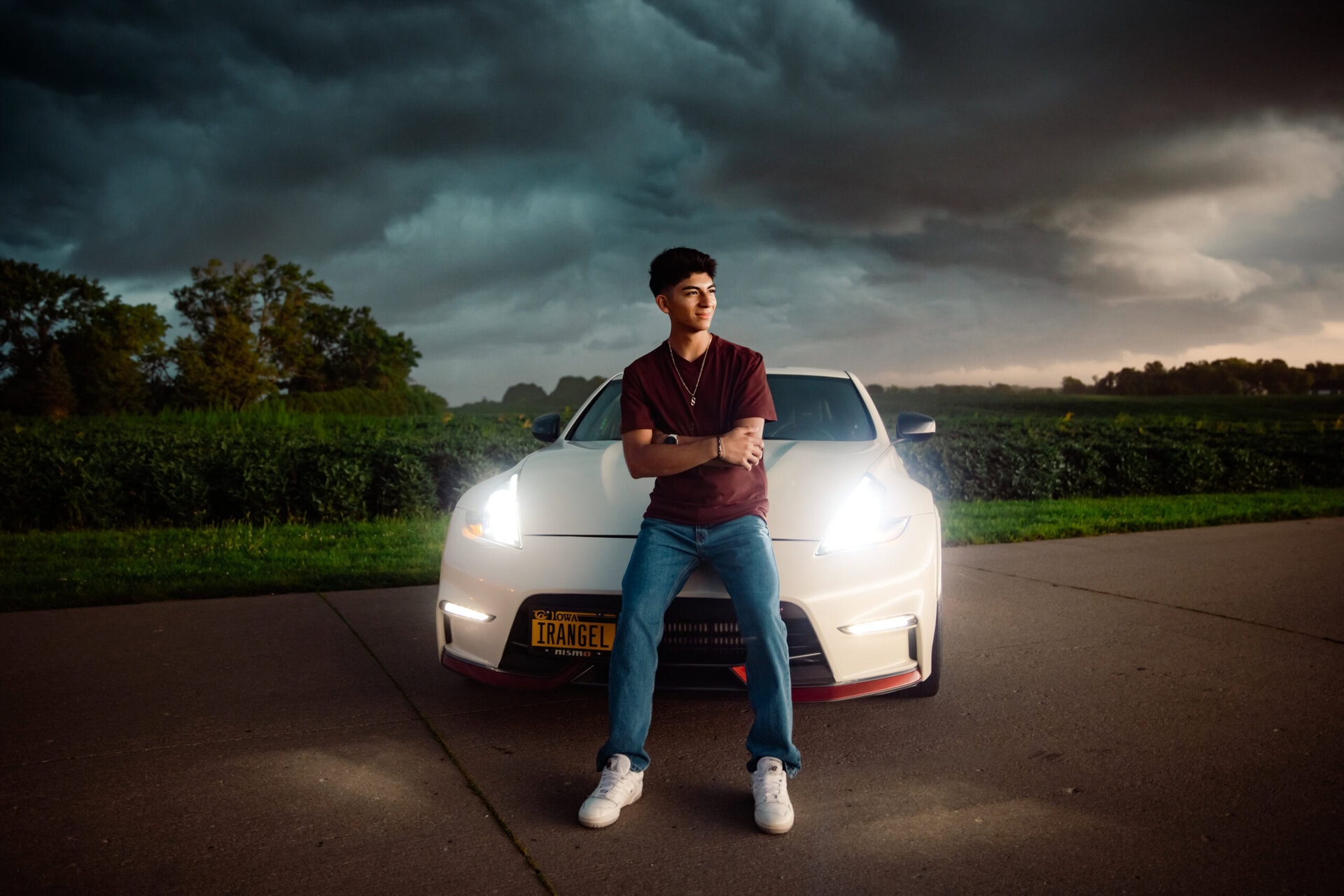 Senior guy leaning on hood of white sports car with headlights on and thunderstorm rolling in background