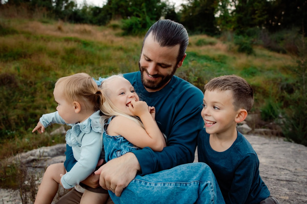 Dad with three kids climbing wildly on his lap