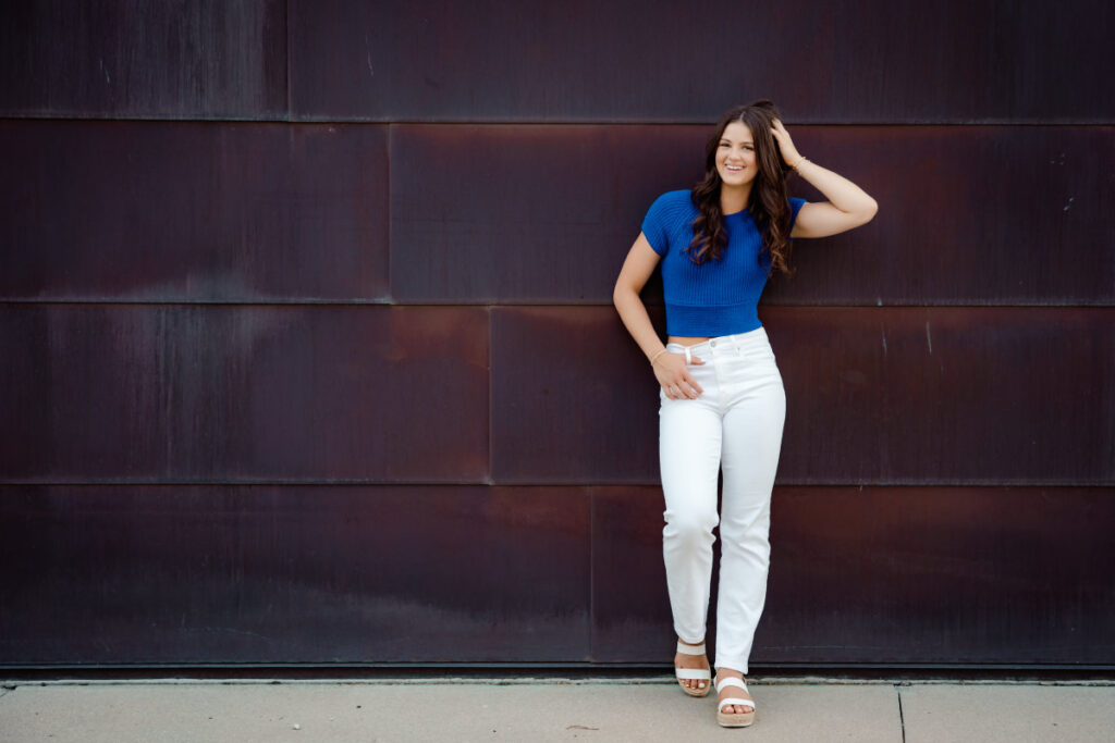 Beginner's guide to senior pictures in Iowa Senior girl in blue top and white jeans leaning against a copper building
