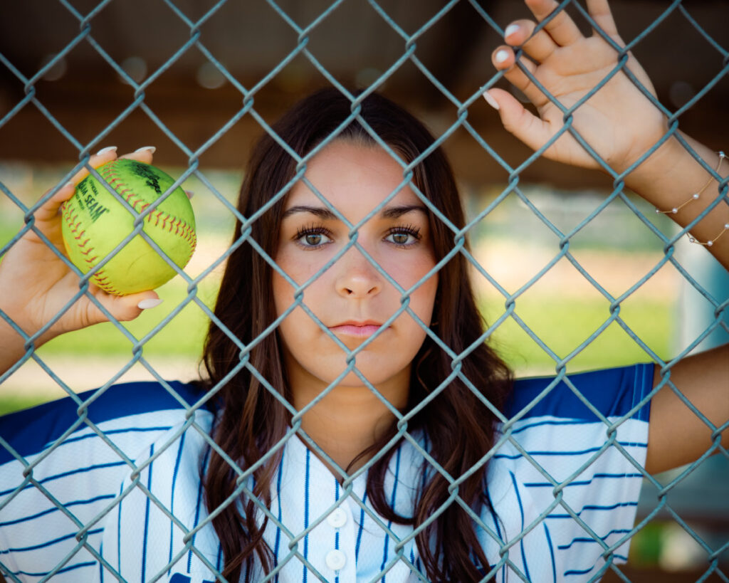 Beginner's guide to senior pictures in Iowa Senior softball player against a fence