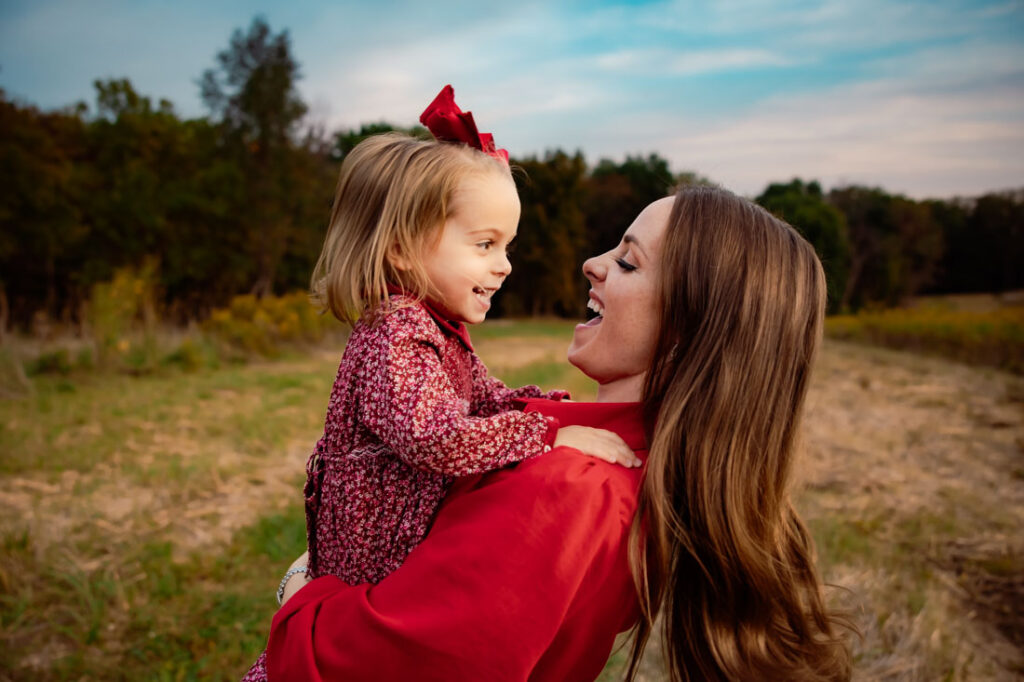 Should I wear my hair down for family photos? Mom holding toddler daughter in a grassy field with her hair moving.