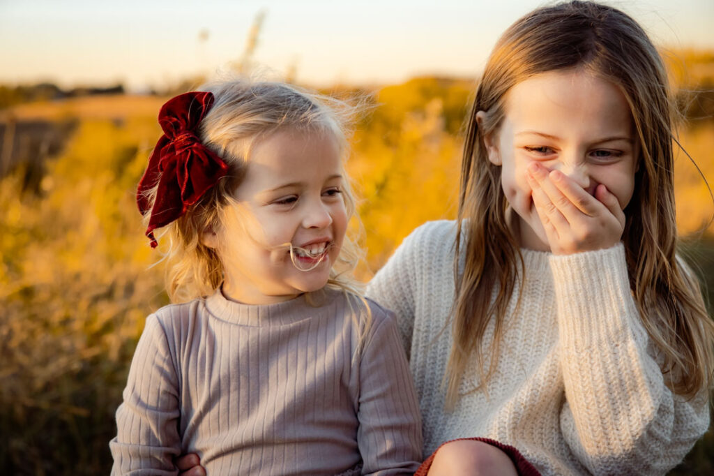 Should I wear my hair down for family photos? Two young sisters sitting next to each other in the fall with wind in their hair.