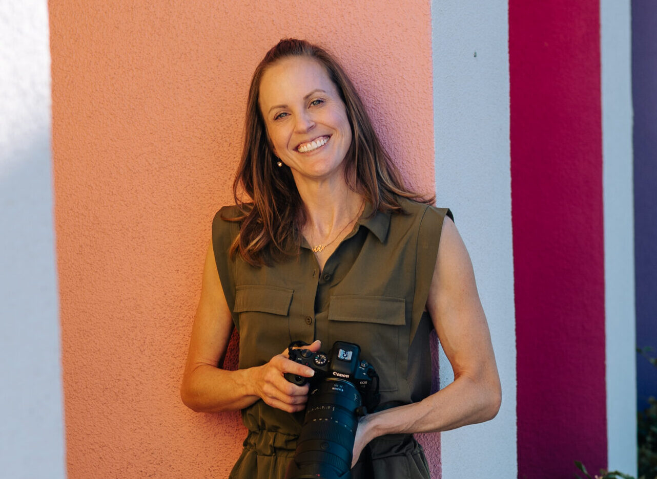Lydia Fine holding a camera leaning against a colorful wall